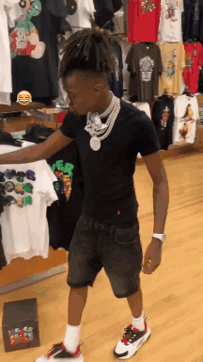 A Young Man In A Black Shirt And Shorts Is Standing In A Store GIF