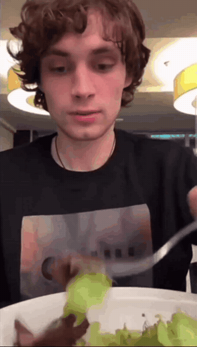 A Young Man In A Black Shirt Is Eating A Salad GIF