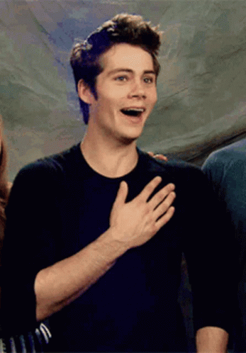 A Young Man In A Black Shirt Is Holding His Hand To His Chest GIF