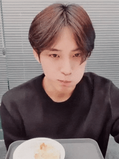 A Young Man In A Black Shirt Is Sitting At A Table With A Bowl Of Food . GIF