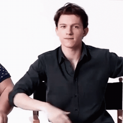 A Young Man In A Black Shirt Is Sitting In A Chair And Making A Funny Face . GIF