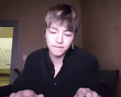 A Young Man In A Black Shirt Is Sitting In A Room With His Eyes Closed And Holding His Hands Together . GIF