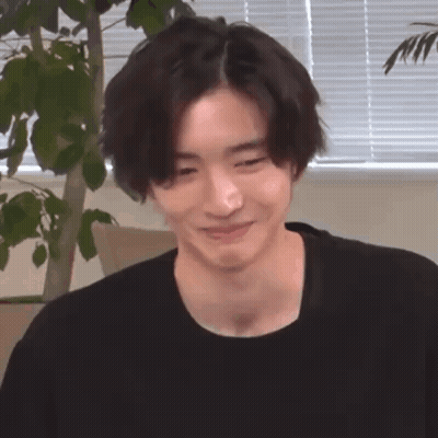 A Young Man In A Black Shirt Is Smiling And Looking At The Camera . GIF