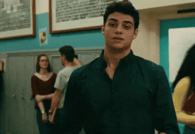 A Young Man In A Black Shirt Is Standing In A Hallway With Other People . GIF