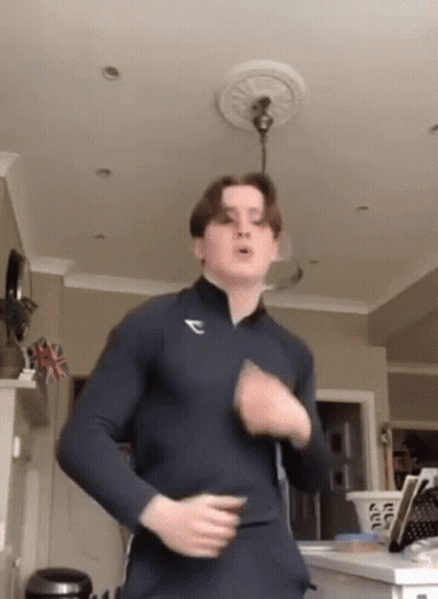 A Young Man In A Black Shirt Is Standing In A Living Room . GIF