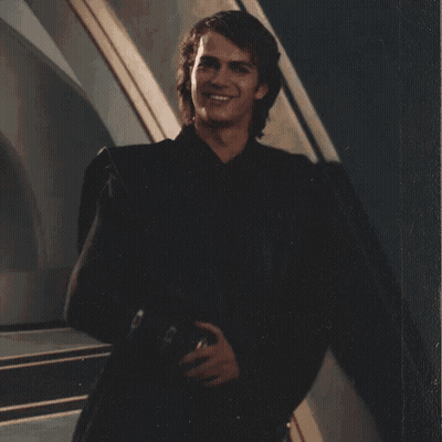 A Young Man In A Black Suit Is Smiling And Holding A Helmet GIF