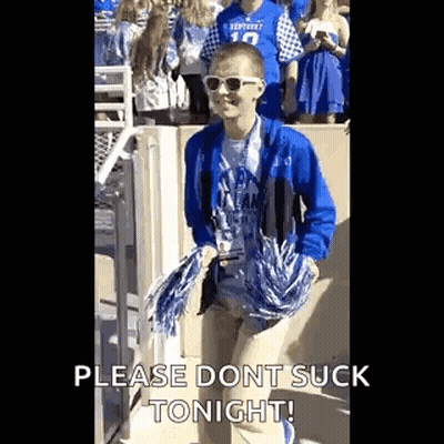 A Young Man In A Blue Jacket And Sunglasses Is Holding Pom Poms And Walking In A Crowd Of People . GIF