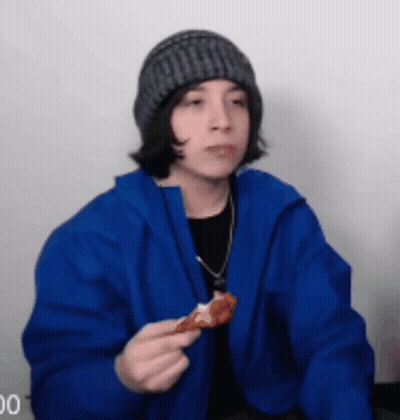 A Young Man In A Blue Jacket Is Eating A Piece Of Pizza . GIF