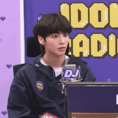 A Young Man In A Blue Jacket Is Sitting In Front Of A Microphone . GIF