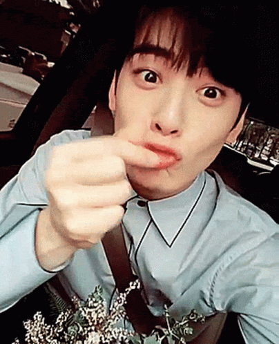 A Young Man In A Blue Shirt Is Holding A Bouquet Of Flowers And Making A Funny Face GIF
