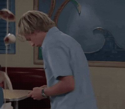 A Young Man In A Blue Shirt Is Looking At His Phone GIF
