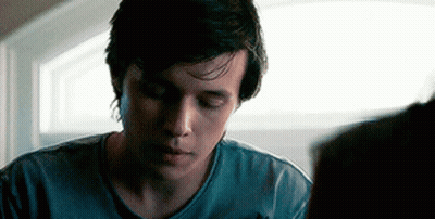 A Young Man In A Blue Shirt Is Looking Down At Something While Sitting In Front Of A Window . GIF
