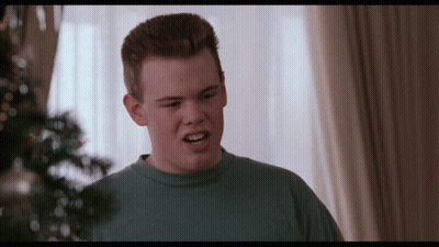 A Young Man In A Blue Shirt Is Making A Face In Front Of A Christmas Tree GIF