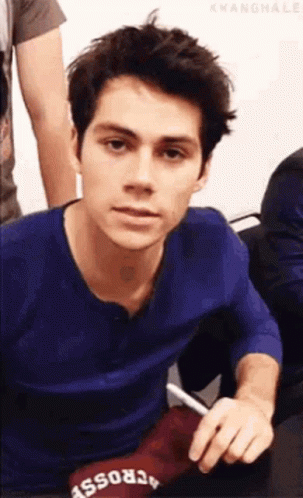 A Young Man In A Blue Shirt Is Sitting Down Holding A Pen . GIF