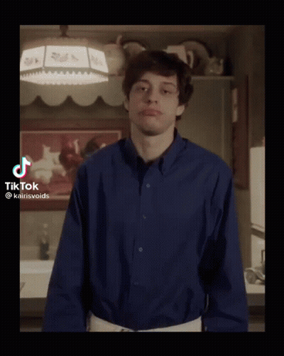 A Young Man In A Blue Shirt Is Standing In A Kitchen With His Arms Outstretched . GIF