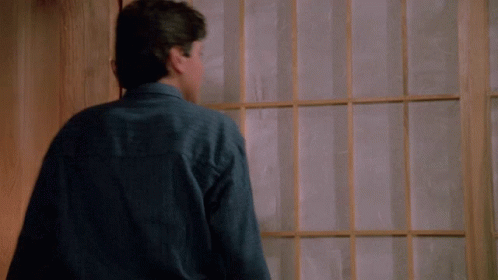 A Young Man In A Blue Shirt Is Standing In Front Of A Window With His Arms Outstretched GIF