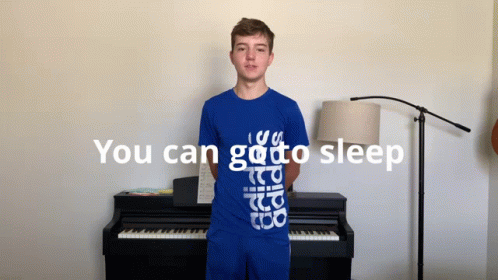 A Young Man In A Blue Shirt Stands In Front Of A Piano With The Words " You Can Go To Sleep " Above Him GIF