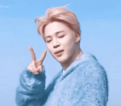 A Young Man In A Blue Sweater Is Making A Peace Sign GIF