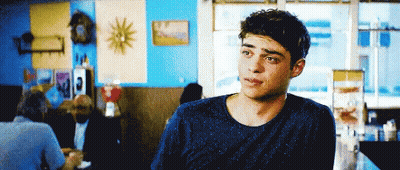 A Young Man In A Blue Sweater Is Sitting At A Table In A Restaurant GIF