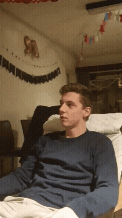 A Young Man In A Blue Sweater Sits On A Chair GIF