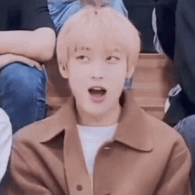 A Young Man In A Brown Jacket Is Sitting In A Crowd With His Mouth Open . GIF