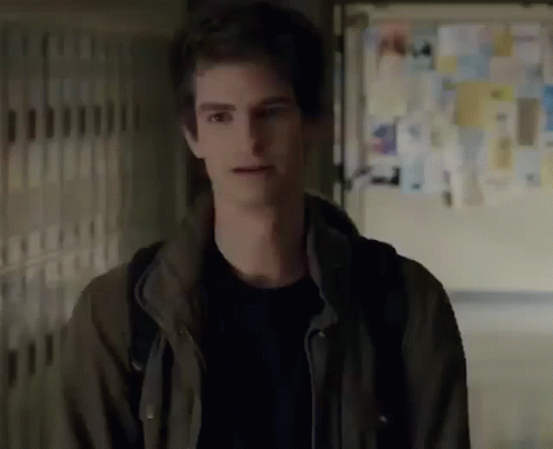A Young Man In A Brown Jacket Is Standing In A Hallway With A Backpack . GIF