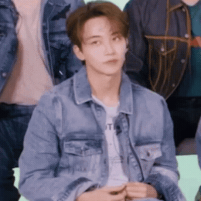 A Young Man In A Denim Jacket Is Sitting In A Group Of People . GIF