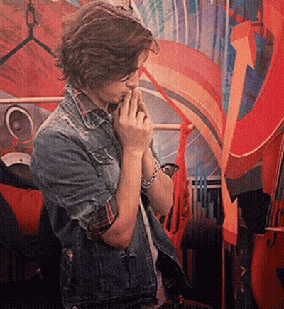 A Young Man In A Denim Jacket Is Standing In Front Of A Colorful Painting GIF