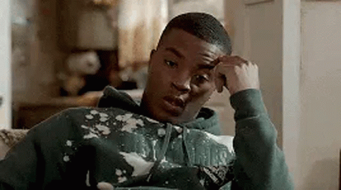 A Young Man In A Green Hoodie Is Sitting On A Couch . GIF