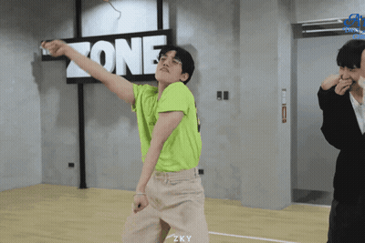 A Young Man In A Green Shirt Is Dancing In Front Of A Sign That Says Zone GIF