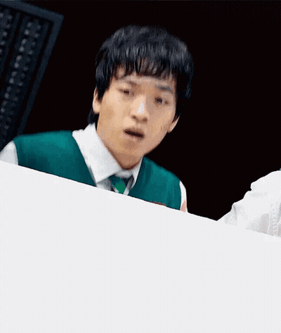 A Young Man In A Green Vest And Tie Is Sitting At A Table With His Mouth Open . GIF