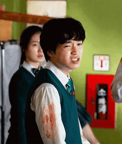 A Young Man In A Green Vest And Tie Is Standing In A Room With Blood On His Shirt . GIF