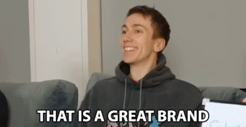 A Young Man In A Hoodie Is Sitting On A Couch And Smiling . GIF