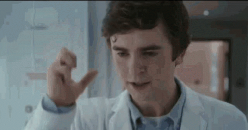 A Young Man In A Lab Coat Is Pointing At Something . GIF