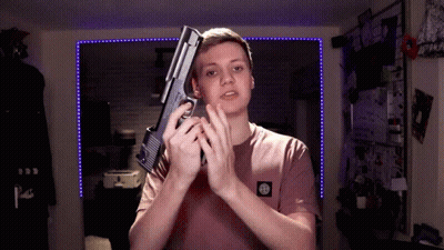 A Young Man In A Pink Shirt Holds A Gun In His Hands GIF
