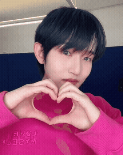 A Young Man In A Pink Shirt Is Making A Heart Shape With His Hands GIF