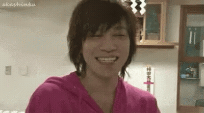 A Young Man In A Pink Shirt Is Smiling With His Eyes Closed In A Room . GIF