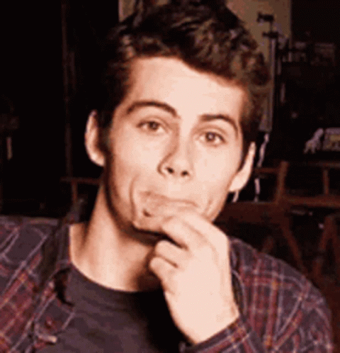 A Young Man In A Plaid Shirt Is Making A Funny Face While Holding His Hand To His Chin . GIF