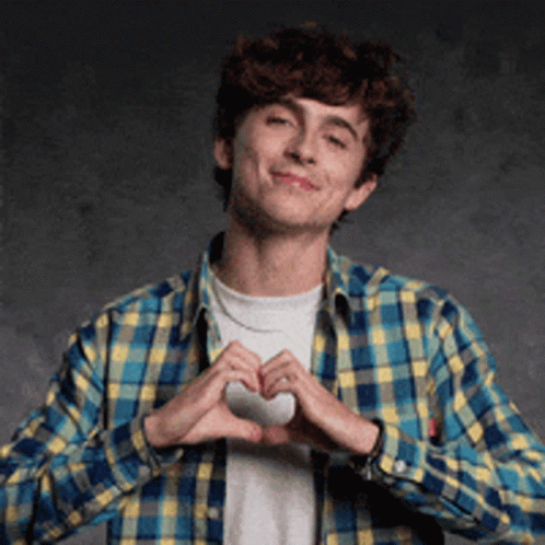 A Young Man In A Plaid Shirt Is Making A Heart With His Hands . GIF