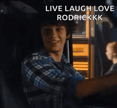 A Young Man In A Plaid Shirt Is Sitting In Front Of A Yellow School Bus With The Words Live Laugh Love Rodrickkkk GIF