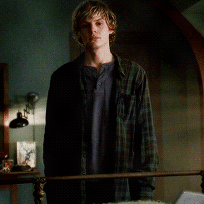 A Young Man In A Plaid Shirt Is Standing Next To A Bed GIF