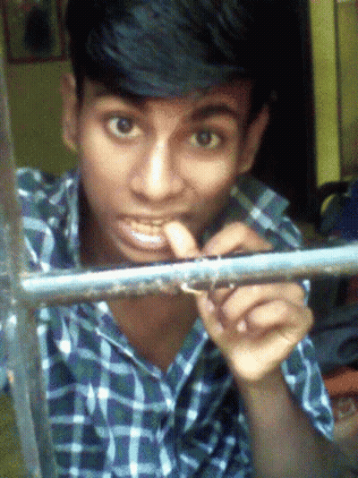 A Young Man In A Plaid Shirt Looks Through A Window GIF