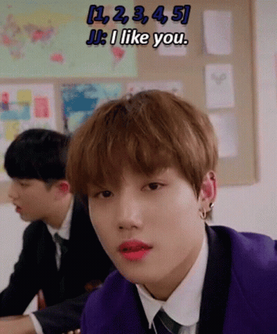 A Young Man In A Purple Suit And Tie Is Sitting At A Desk In A Classroom With Other Students . GIF