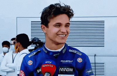 A Young Man In A Racing Suit Is Talking Into A Microphone And Smiling . GIF