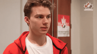 A Young Man In A Red Jacket Is Standing In Front Of A Poster That Says Canada GIF