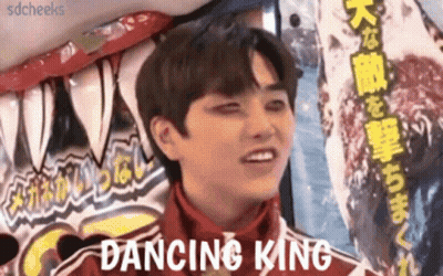 A Young Man In A Red Jacket Is Standing In Front Of A Sign That Says Dancing King . GIF