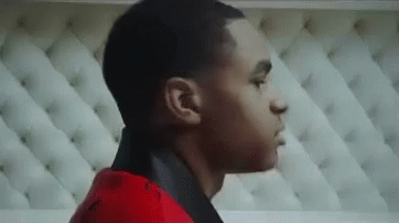 A Young Man In A Red Jacket Is Standing In Front Of A White Couch . GIF