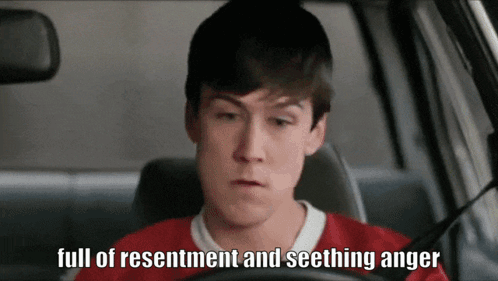 A Young Man In A Red Shirt Is Driving A Car With The Words Full Of Resentment And Seething Anger Below Him GIF