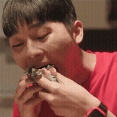 a young man in a red shirt is eating a sandwich