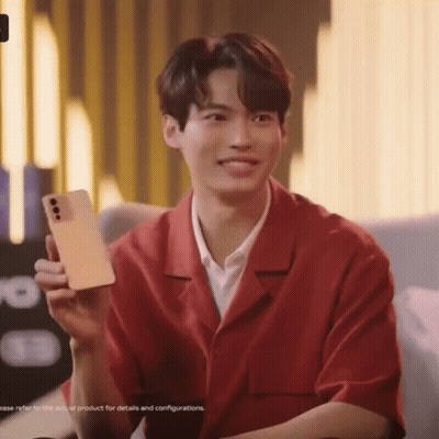 A Young Man In A Red Shirt Is Holding A Cell Phone In His Hand . GIF